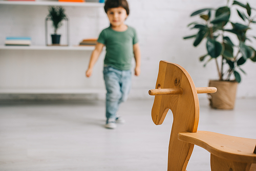 Selective focus of toddler boy in green t-shirt and wooden rocking horse