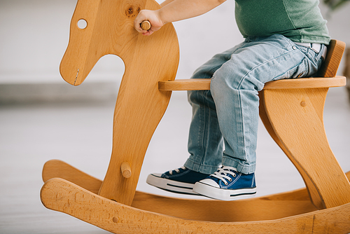 cropped view of child sitting on wooden rocking horse in living room