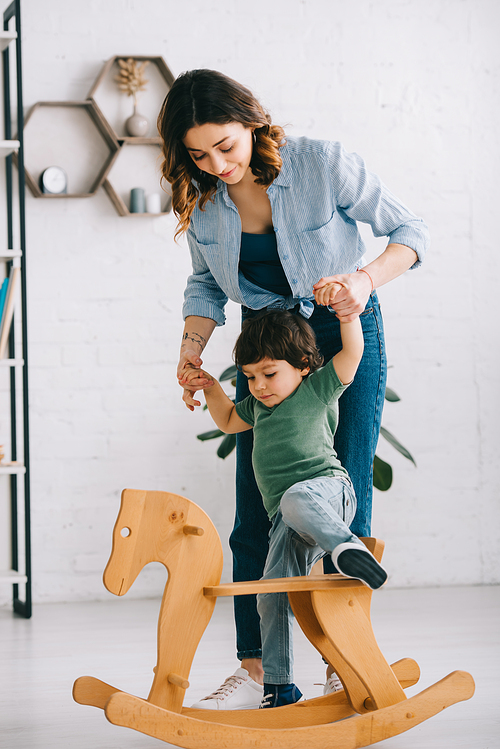 Kid on rocking horse holding hands with mom in living room