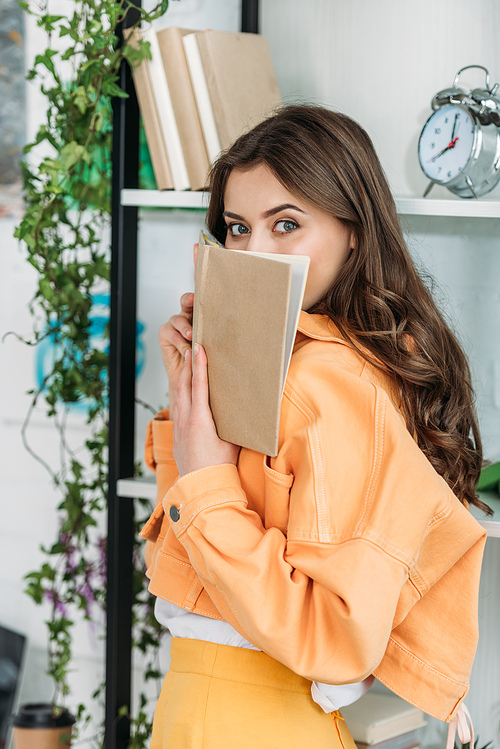 attractive young woman  while covering face with book