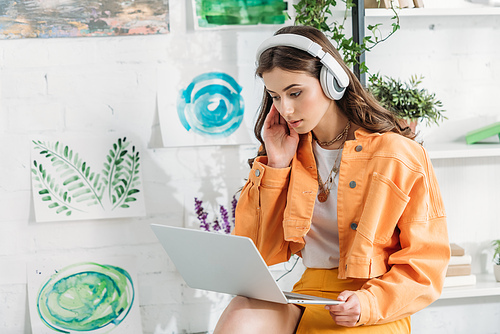 attentive pretty girl using laptop while listening music in headphones