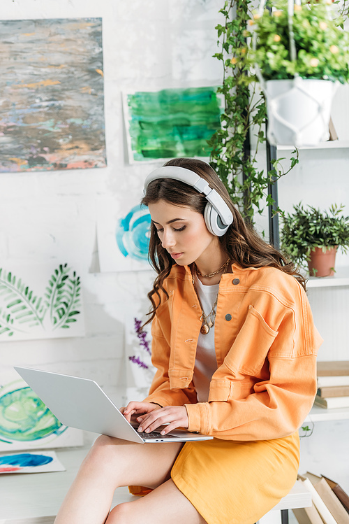 attentive girl in headphones using laptop while sitting on desk at home