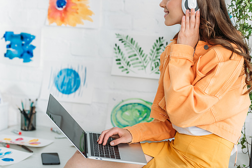 partial view of young woman listening music in headphones and using laptop