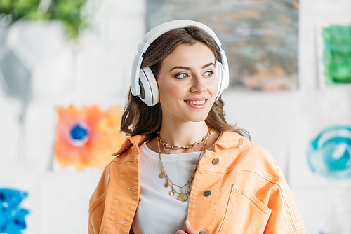 fashionable young woman in necklace listening music in headphones and looking away