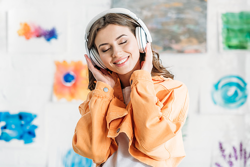 happy young woman in orange jacket listening music in headphones with closed eyes