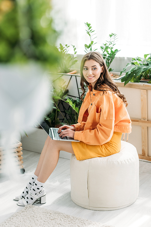 selective focus of happy young woman sitting on pouf and using laptop at home