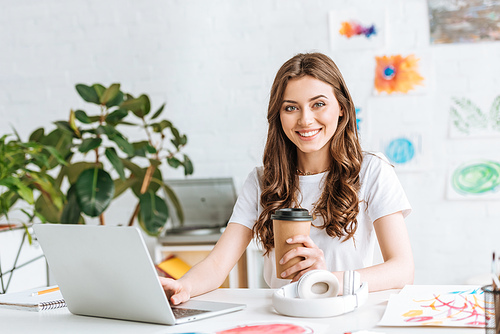 smiling young woman  while using laptop and holding disposable cup