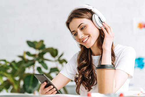 smiling young woman listening music in headphones and using smartphone at home