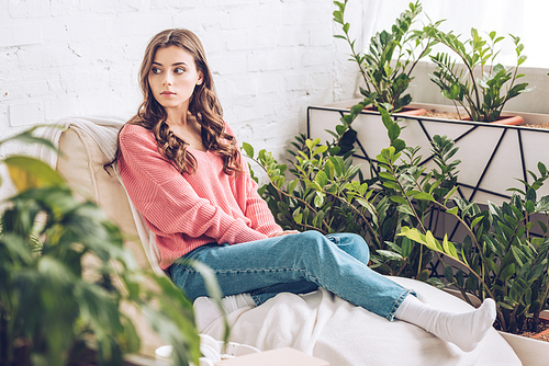 selective focus of pensive young woman sitting in room near lush green plants