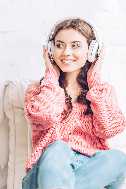 cheerful young woman listening music in headphones and looking away