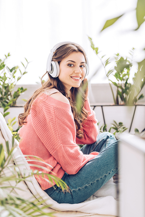 attractive young woman listening music in headphones and  while sitting surrounded by green plants at home