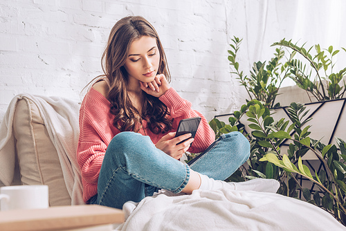 thoughtful young girl using smartphone while sitting with crossed legs