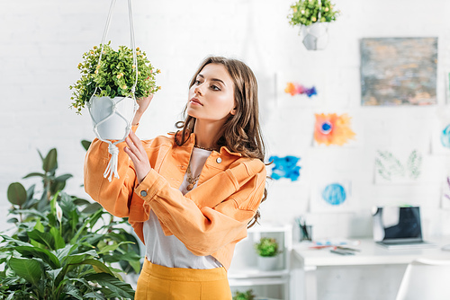 beautiful woman in orange clothing touching hanging flowerpot at home