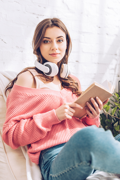 attractive young woman with book and headphones  while sitting with crossed legs