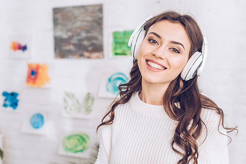 beautiful cheerful girl listening music in headphones and smiling at camera
