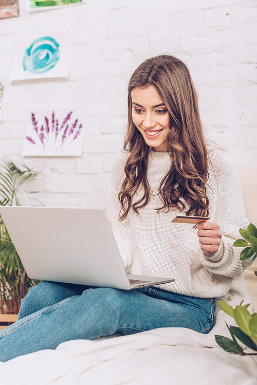 cheerful young woman using smartphone and holding credit card