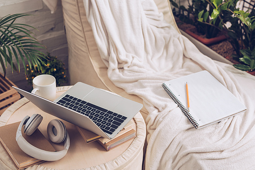 laptop, headphones, books and coffee cup on pouf near soft chaise lounge