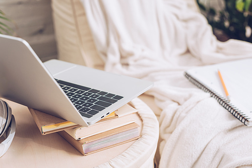 selective focus of laptop and books near soft white chaise lounge covered with white blanket