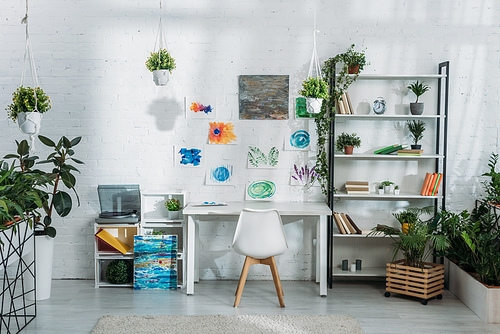 light spacious room decorated with plants and paintings on white wall with racks, desk and chair