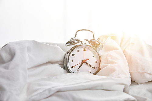 silver alarm clock on blanket in white bed with sunlight on background