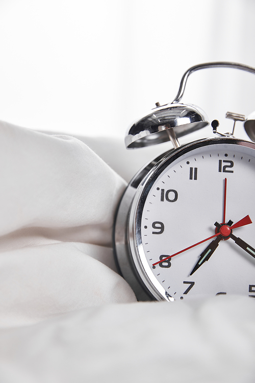 close up view of silver alarm clock in white bed