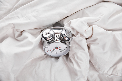 top view of silver alarm clock in white bed