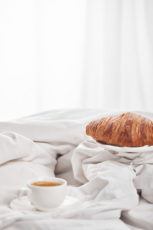 delicious croissant on plate near coffee in white cup on saucer in bed