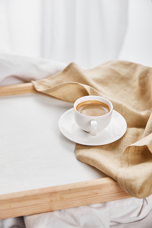 coffee in white cup on saucer near beige napkin on wooden tray