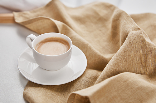 close up view of coffee in white cup on saucer near beige napkin