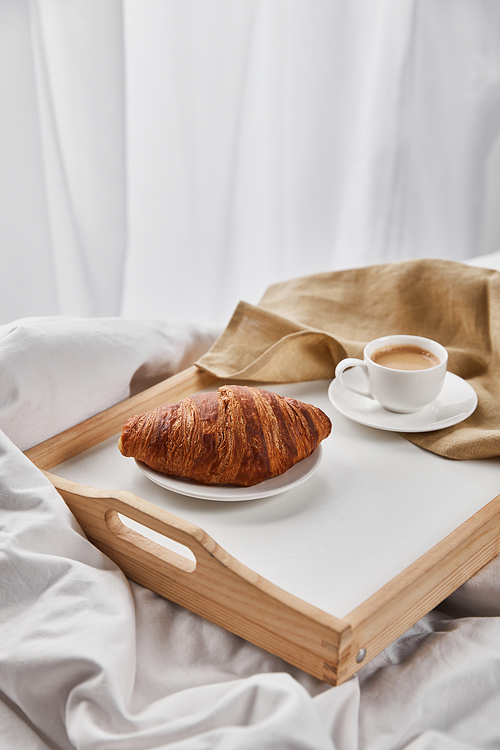 fresh croissant with coffee on wooden tray with beige napkin
