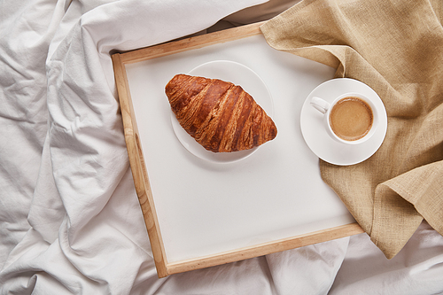 top view of fresh croissant with coffee on wooden tray in bed at morning