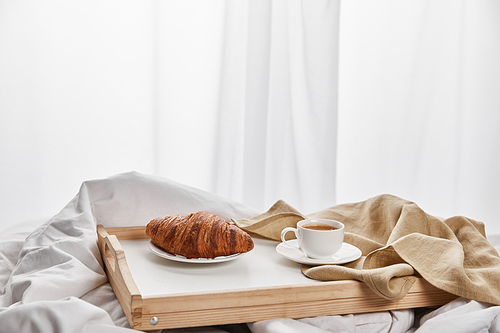fresh croissant with coffee in cup on wooden tray in bed at morning