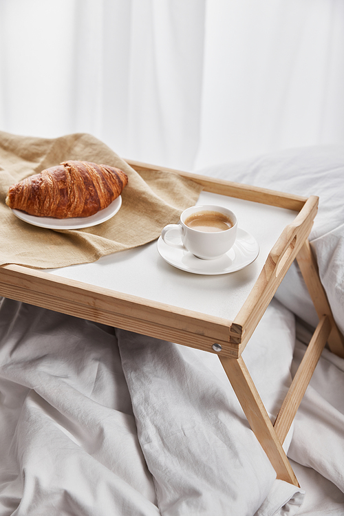 fresh croissant with coffee on wooden tray in bed at morning