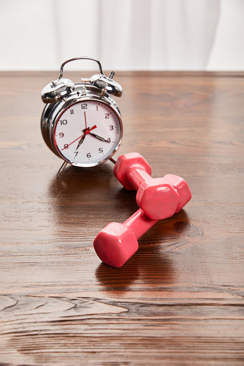 silver alarm clock near pink dumbbells on wooden table
