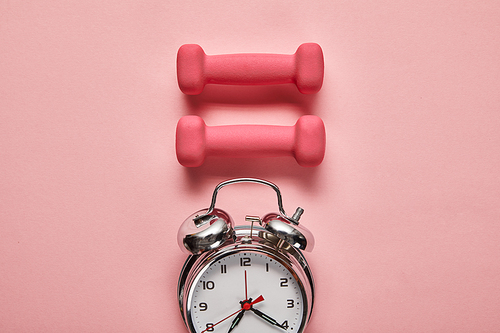 flat lay with silver alarm clock and pink dumbbells on pink background