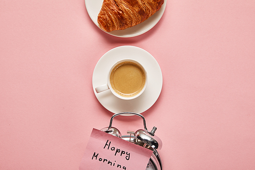 flat lay with alarm clock with happy morning lettering on sticky note near coffee and croissant on pink background