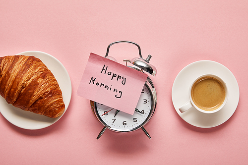 top view of alarm clock with happy morning lettering on sticky note near coffee and croissant on pink background