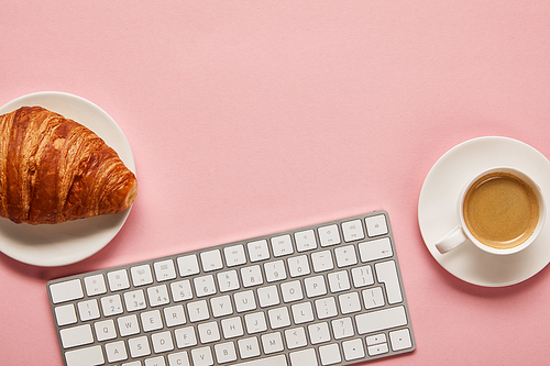 top view of computer keyboard near coffee and tasty croissant on pink background