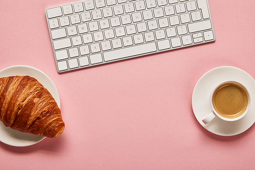 top view of computer keyboard near coffee and croissant on pink background