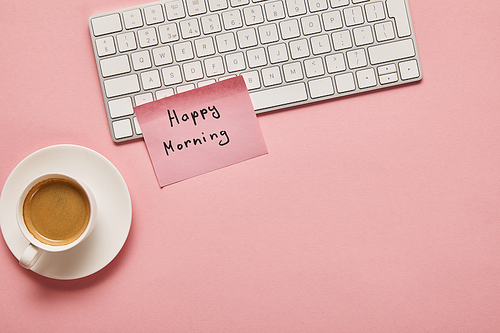 top view of computer keyboard and pink sticky note with happy morning lettering near coffee on pink background