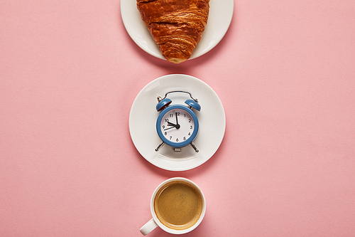 flat lay with coffee cup, toy alarm clock and croissant on plate on pink background