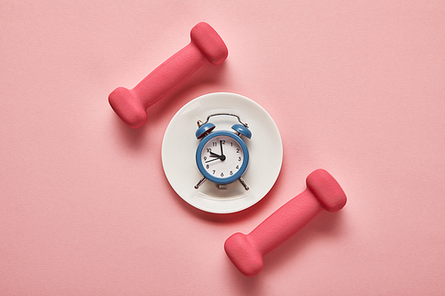 top view of dumbbells and plate with toy alarm clock on pink background
