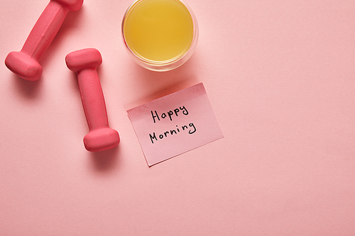 top view of orange juice, pink dumbbells and sticky note with happy morning lettering on pink background