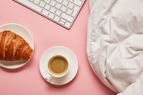top view of blanket, computer keyboard, coffee and croissant on pink background