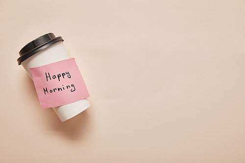 top view of coffee to go and sticky note with happy morning lettering on beige background