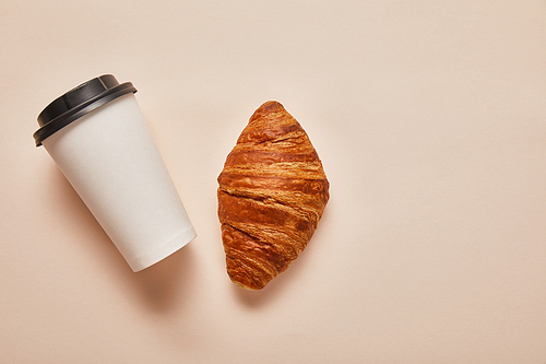 top view of coffee to go and tasty croissant on beige background