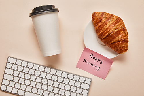 top view of coffee to go, croissant, computer keyboard and sticky note with happy morning lettering on beige background