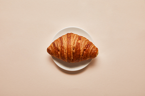 top view of tasty croissant on white plate on beige background