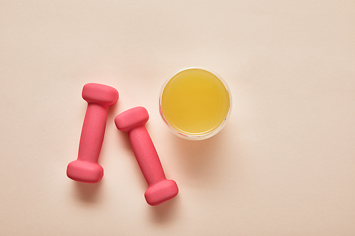 top view of pink dumbbells, orange juice on beige background