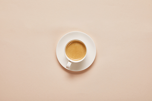 top view of coffee in cup on saucer on beige background